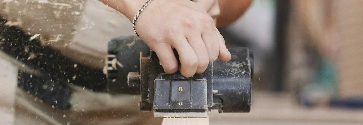 Person hobelt Holz mit Elektrohobel